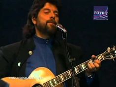 a man with long hair and beard playing an acoustic guitar in front of a microphone