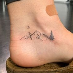 a small tattoo on the foot of a person with mountains and trees in the background