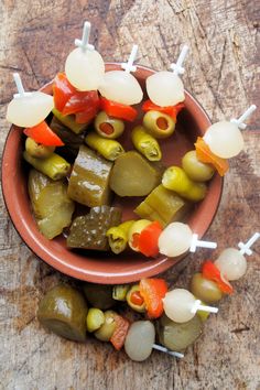 several skewered vegetables in a clay bowl on a wooden table with toothpicks sticking out of them