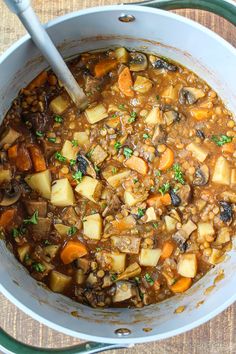 a white bowl filled with stew and vegetables on top of a wooden table next to a spoon