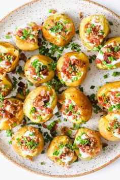 a white plate topped with mini potatoes covered in bacon and sour cream, garnished with chopped green onions