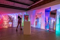 a woman standing in front of an art exhibit with colorful lights on the walls and behind her