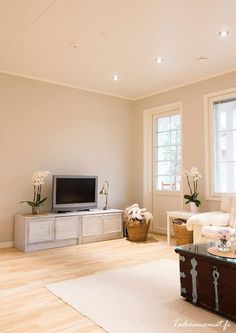 a living room with white furniture and flowers on the coffee table in front of a flat screen tv