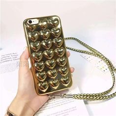 a hand holding a gold phone case with hearts on the front and sides, while it is