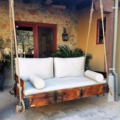 a white couch sitting on top of a wooden swing bed next to a door and potted plant