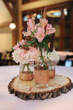 pink flowers are in mason jars on a wood slice for centerpieces at a wedding reception