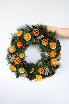 a wreath with oranges and pine cones is being held by someone's hand