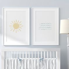 a white crib with two pictures on the wall above it and a lamp next to it