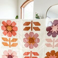 three quilts are hanging on the wall in front of a mirror and potted plant