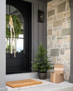 a christmas tree is sitting on the front porch next to a box and a wreath