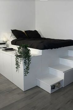 a bed sitting on top of a wooden floor next to a white shelf filled with plants