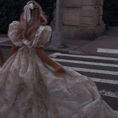 a woman in a long dress is walking across the street with her back to the camera