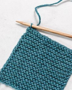 a blue knitted square with a wooden knitting needle