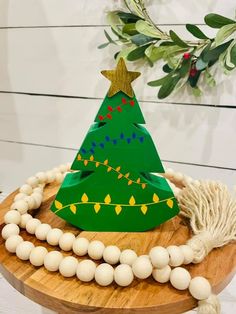 a paper christmas tree on top of a wooden board with beads around it and greenery in the background