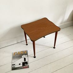 a small wooden table sitting on top of a hard wood floor next to a magazine