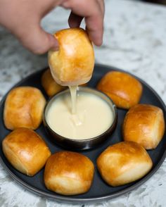 a person dipping some food into a bowl on top of a black plate with rolls