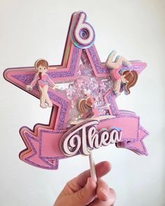 a hand holding up a pink and purple star shaped cake topper with the word there on it