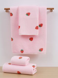 pink towels with strawberries on them are hanging from a towel rack next to two folded ones