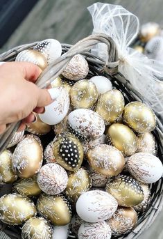 a basket filled with gold and white decorated eggs on top of a wooden table next to a person