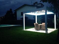 an outdoor dining area lit up at night with lights on the table and chairs in the foreground