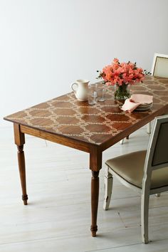 a wooden table with two chairs and a vase on top of it next to a white wall