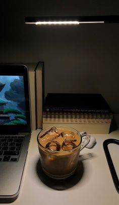 a laptop computer sitting on top of a desk next to a cup filled with liquid