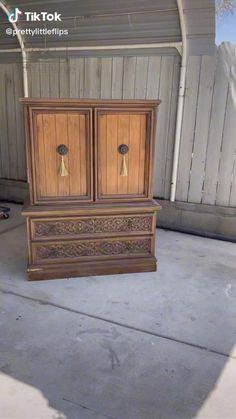 an old wooden cabinet sitting in the middle of a driveway next to a garage door