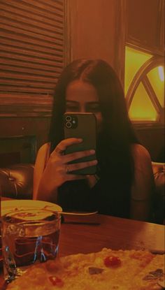 a woman sitting at a table taking a selfie with her cell phone while eating pizza