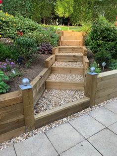 wooden steps leading up to the top of a garden area with gravel and flowers around them