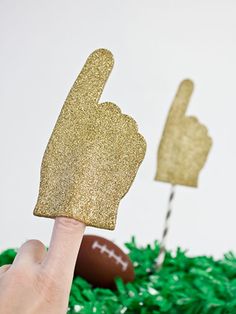 a hand is pointing at a football on top of green grass with two thumbs up