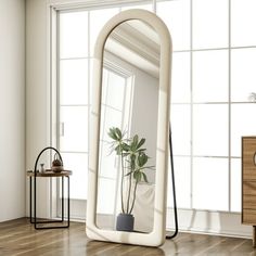 a large mirror sitting on top of a wooden floor next to a table with a potted plant