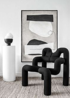 a black and white painting sitting next to a chair in front of a large art piece