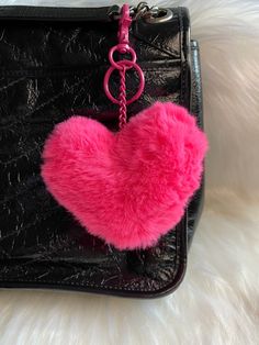 a pink heart shaped pom - pom keychain hanging from a black purse