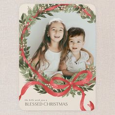 two children are sitting in front of a christmas card with a red bow on it