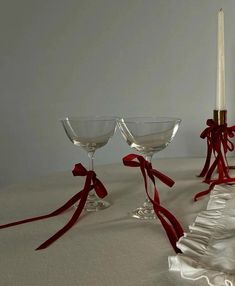 three wine goblets with red ribbons tied around them on a white tablecloth