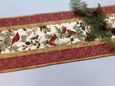 a table runner with red birds and pine cones on it, hanging from a wall