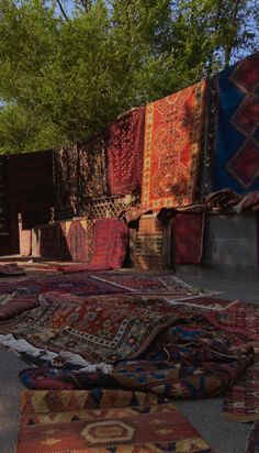 many rugs and carpets are laid out on the ground in front of some trees