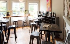 an empty restaurant with wooden tables and stools in front of large windows, filled with wine bottles