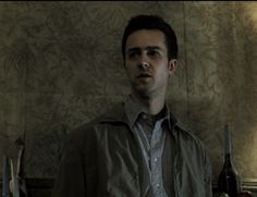 a man standing in front of a wall with wine bottles on the table behind him