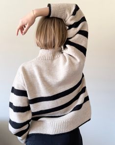 a woman wearing a white and black striped sweater with her hands on the back of her head