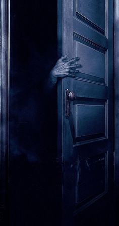 a person's hand coming out of an open door into a dark room with fog