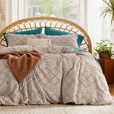 a bed covered in a blanket and pillows next to a window with potted plants