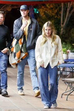 two men and a woman walking down a sidewalk with one man in the background wearing jeans