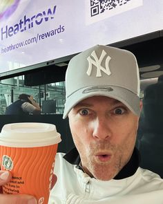 a man holding up a cup of coffee in front of a sign with the new york yankees on it