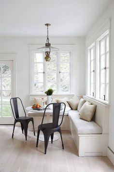 two chairs and a table in a room with white walls, wood floors and windows