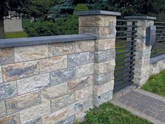 a stone wall with metal railings next to a brick walkway in front of some trees