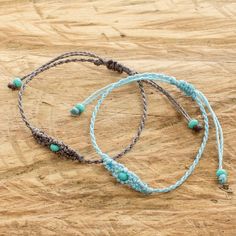 two braided bracelets with turquoise beads are on a wooden surface and one has a small bead in the middle