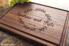 a wooden cutting board with the name and date engraved on it next to some flowers