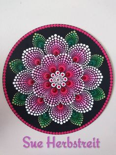 a colorful flower painted on a black and pink circle with the words sue herbstreit