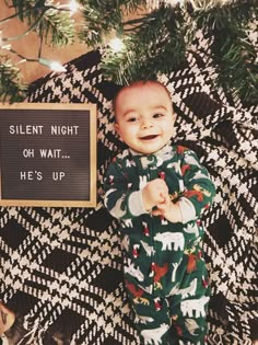 a baby in pajamas standing next to a sign that says silent night of wait me's up